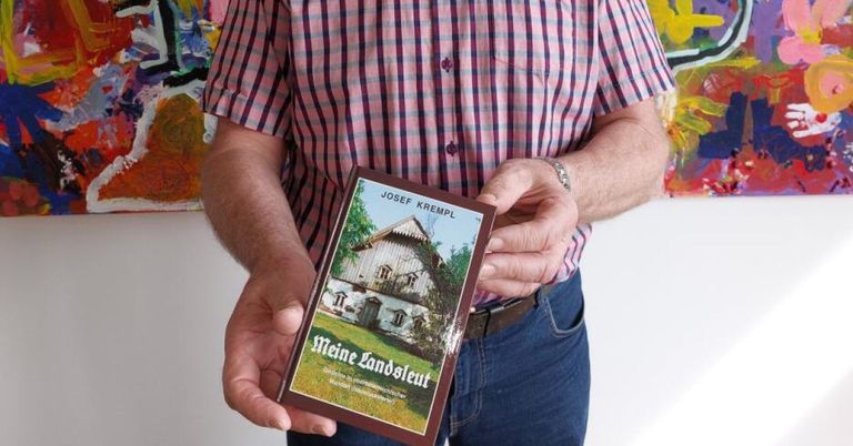 Ein Mann in einem karierten Hemd hält ein Buch mit dem Titel 'Meine Landschleif' von Josef Krempl, das ein Bild eines Hauses zeigt.