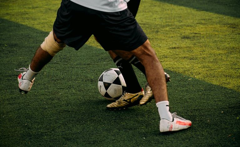 Fußballspieler in schwarzen Shorts und weißen Socken tritt einen Fußball auf einem grünen Feld.