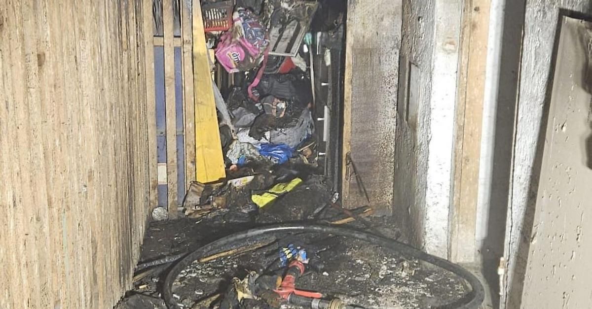 A cluttered and burnt-out room with debris scattered around, a fire hose lying on the ground, and remnants of a fire extinguisher.