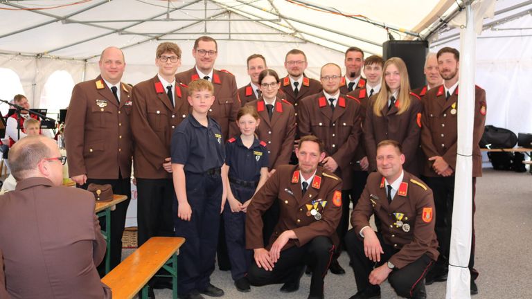 Eine Gruppe von Menschen in braunen Uniformen posiert für ein Foto, wobei einige vorne knien und andere dahinter stehen. Es gibt zwei kleine Kinder vorne, und sie alle lächeln.