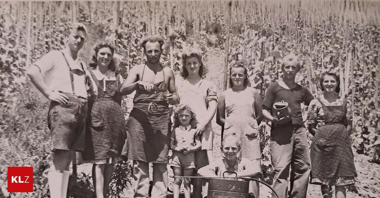 A group of people, including women, a man, and a child, are standing in a field of tall plants, smiling.