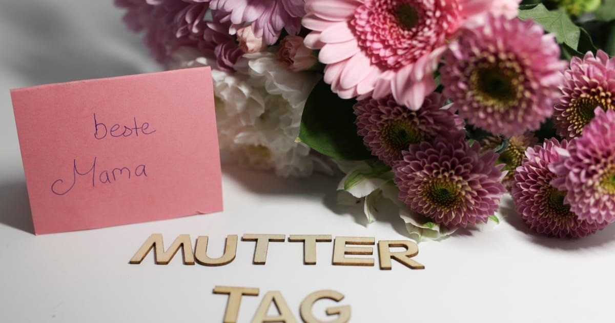 Eine rosa Karte mit dem Wort 'Mutter' darauf, neben einem Strauß aus rosa und weißen Blumen.