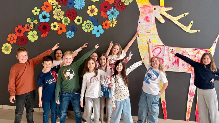 Eine Gruppe von Kindern posiert für ein Foto vor einer bunten Blumenwand und einem Giraffen-Mural im Hintergrund.