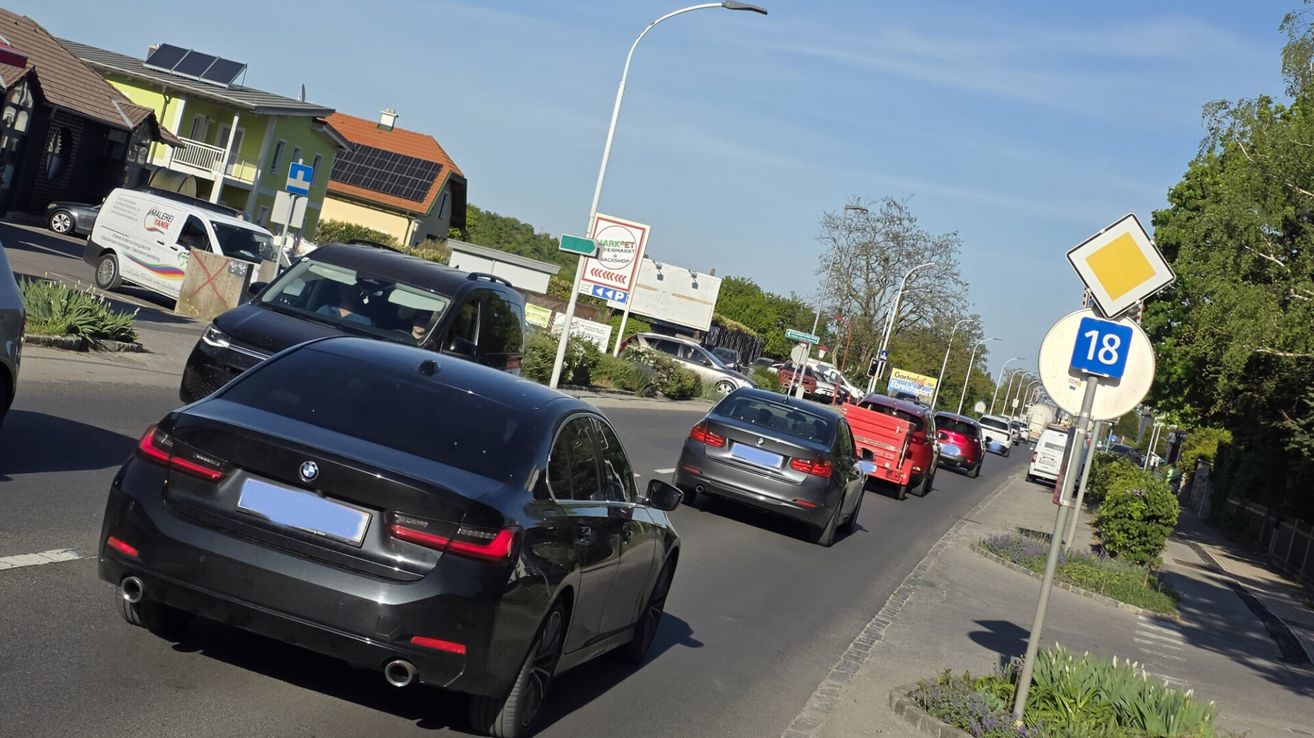 A street with several cars, including a black BMW and a gray BMW, is lined with streetlights. A house with solar panels on the roof is on the left.