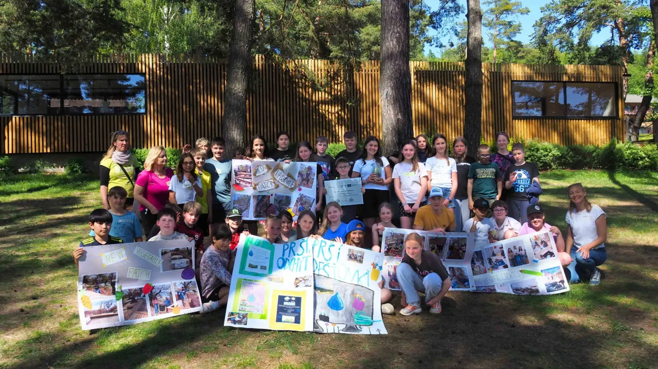 Eine Gruppe von Kindern und Erwachsenen posiert mit Plakaten und Schildern in einem Park. Einige der Kinder halten Schilder und einige tragen Mützen.