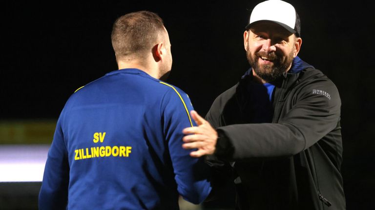 Zwei Männer unterhalten sich; einer trägt ein blaues Shirt mit SV ILLINGDORF, der andere hat eine schwarze Jacke und eine weiße Kappe.