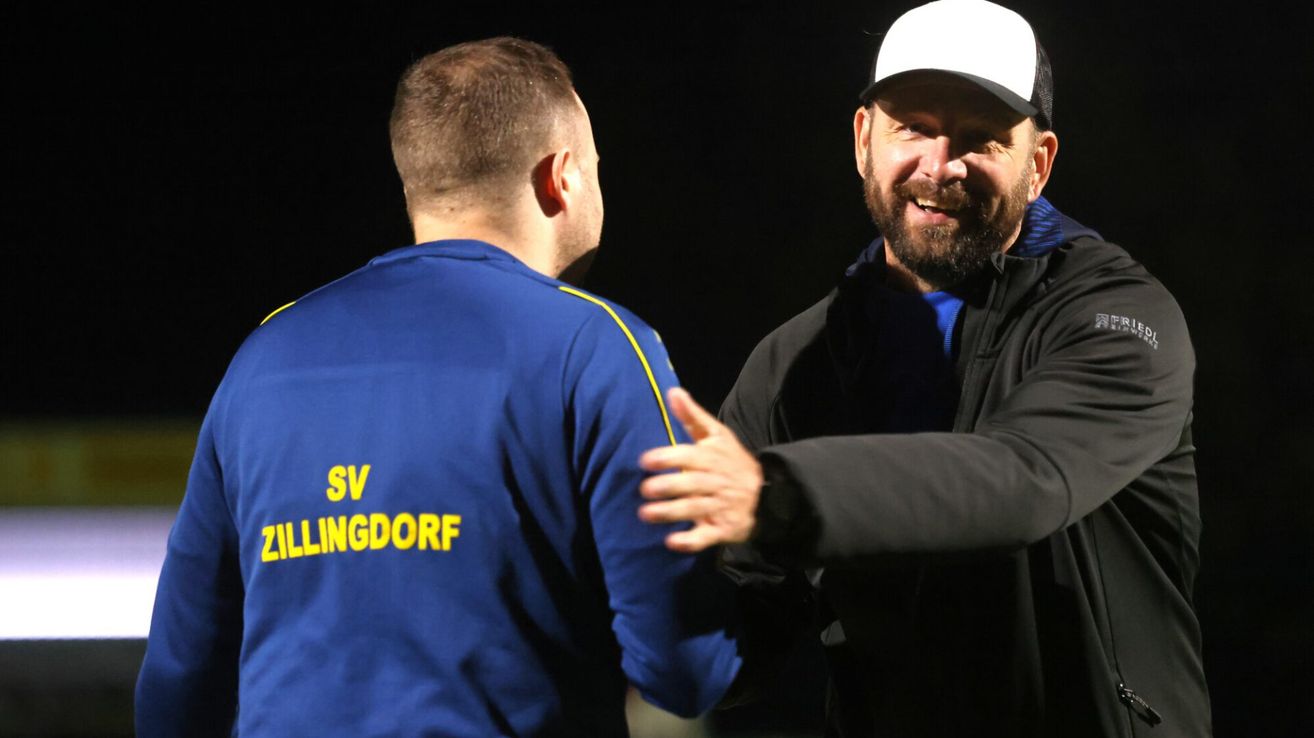 Zwei Männer unterhalten sich; einer trägt ein blaues Shirt mit SV ILLINGDORF, der andere hat eine schwarze Jacke und eine weiße Kappe.