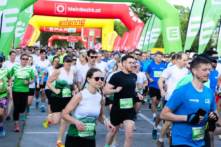 Ein Marathon mit Teilnehmern, die verschiedene Laufnummern tragen. Sie laufen auf einer Straße mit grünen und roten Bögen. Viele Menschen nehmen am Marathon teil.