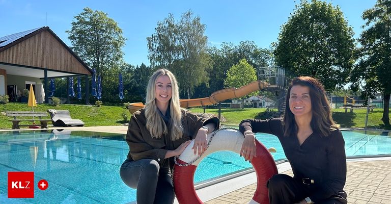 Zwei Frauen posieren neben einem Pool mit einem Rettungsring, eine lächelt und hält ihn, ein Wasserrutsche und grüne Bäume im Hintergrund.
