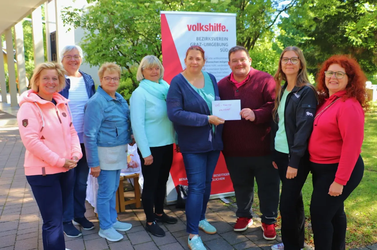 Eine Gruppe von Menschen steht vor einem Banner mit der Aufschrift volkshilfe. Die Frau in der Mitte hält ein Zertifikat.