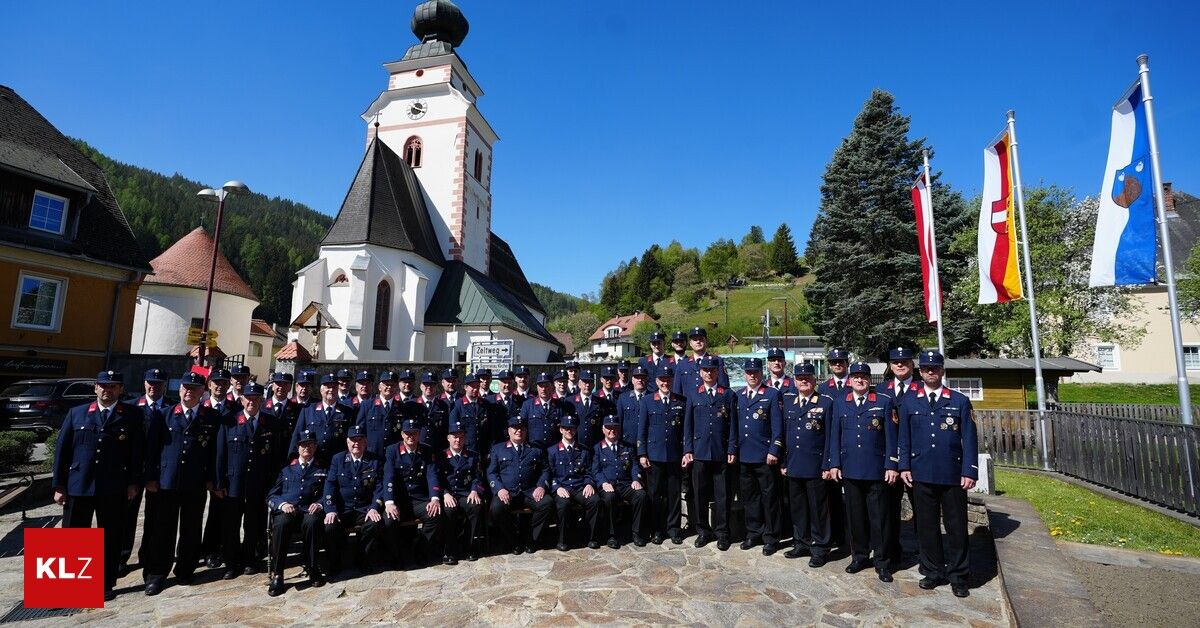 Eine Gruppe uniformierter Personen, möglicherweise Polizei, steht und sitzt vor einer Kirche mit einer Flagge auf einem Mast im Hintergrund.
