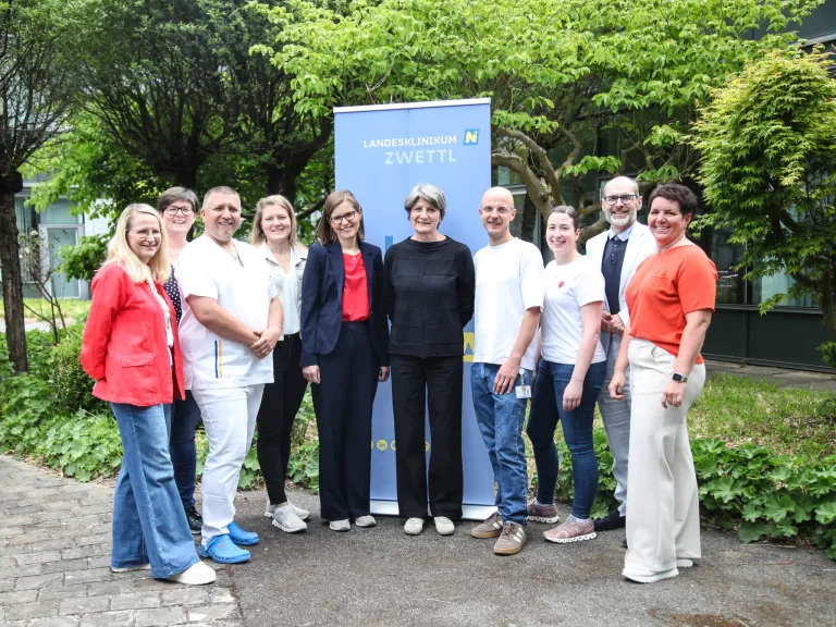 Eine Gruppe von Menschen, einschließlich Gesundheitsfachkräften und Offiziellen, steht zusammen vor einem Banner für das Landesklinikum Zwettl. Sie alle lächeln für die Kamera.