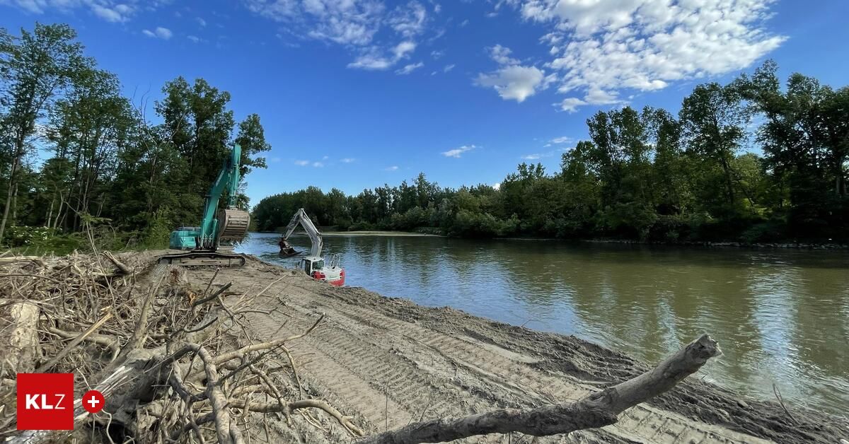 Ein blauer Himmel mit verstreuten Wolken über einem Fluss mit zwei Baggern am Ufer. Bäume säumen das Flussufer.