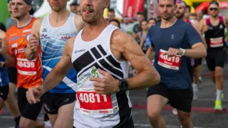 Ein Marathon mit Läufern, einer vorne mit der Nummer 40811. Dahinter folgen weitere Läufer. Sie tragen alle Laufausrüstung. Hinter den Läufern befinden sich orange und grüne Aufblasbare.