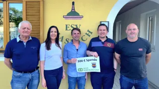 Fünf Personen posieren für ein Foto vor einer gelben Wand mit 'ESV' und 'Aspach' darauf. Ein Mann hält ein Schild mit '300 € Spende SOS Kinderdorf'.