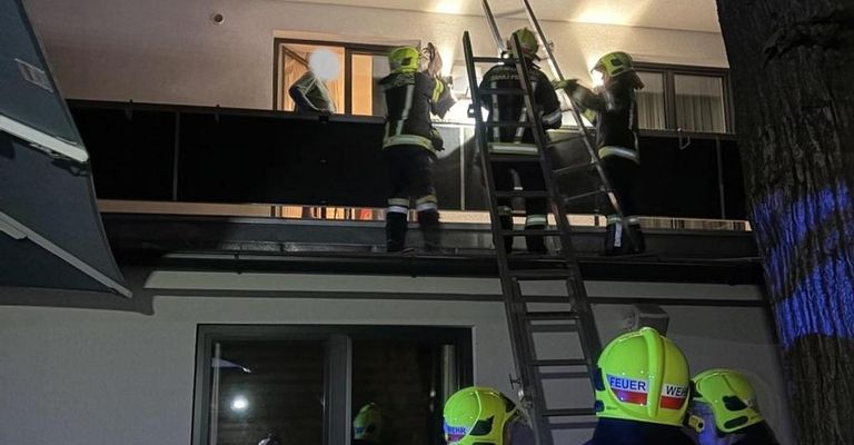 Feuerwehrleute in Sicherheitsausrüstung stehen auf dem Dach, zwei benutzen Leitern und einer steht am Rand. Einer hält eine Taschenlampe und ein anderer ist in der Nähe eines Fensters.