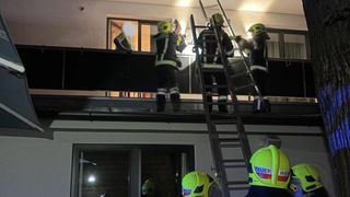 Feuerwehrleute in Sicherheitsausrüstung stehen auf dem Dach, zwei benutzen Leitern und einer steht am Rand. Einer hält eine Taschenlampe und ein anderer ist in der Nähe eines Fensters.