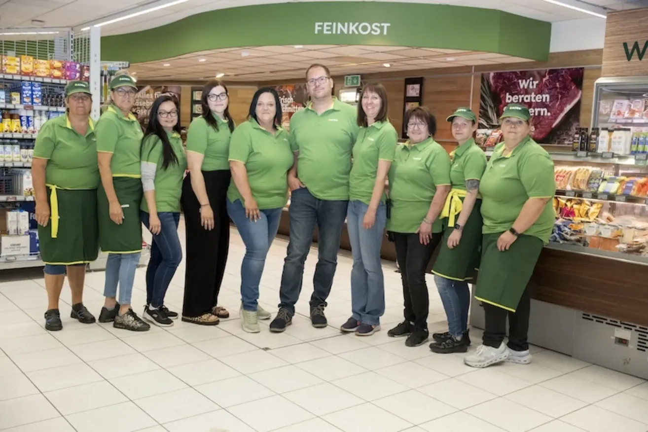 Eine Gruppe von Menschen in grünen Uniformen posiert für ein Foto in einem Feinkost-Geschäft.
