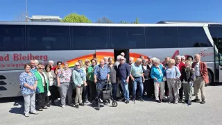 Eine Gruppe älterer Menschen steht an einem sonnigen Tag vor einem Bus. Sie alle lächeln und einige benutzen Gehhilfen.
