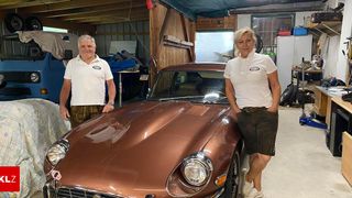 Zwei Personen in einer Garage mit einem braunen Oldtimer, ein Mann und eine Frau tragen passende weiße Poloshirts.
