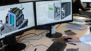 Zwei Monitore zeigen 3D-Modelle, einer mit einer Leiterplatte und ein anderer mit einem mechanischen Design. Eine Hand benutzt eine Computermaus.