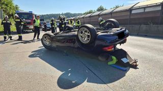 Ein umgestürztes Auto auf einer Autobahn, bei dem mehrere Personen in gelben Westen die Situation behandeln, einschließlich eines Feuerwehrmanns.