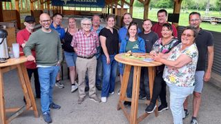 Eine Gruppe von Menschen steht draußen und lächelt, während sie für ein Foto posieren. Ein Tisch mit Essen steht im Vordergrund. Ein Volksbank-Banner hängt im Hintergrund.