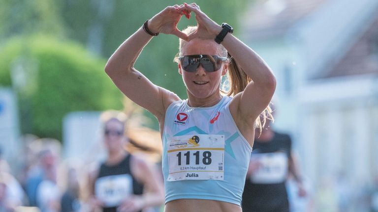 Eine Läuferin namens Julia, die eine Sonnenbrille und einen Nummernaufkleber 1118 trägt, bildet während eines Marathons mit ihren Händen ein Herz.