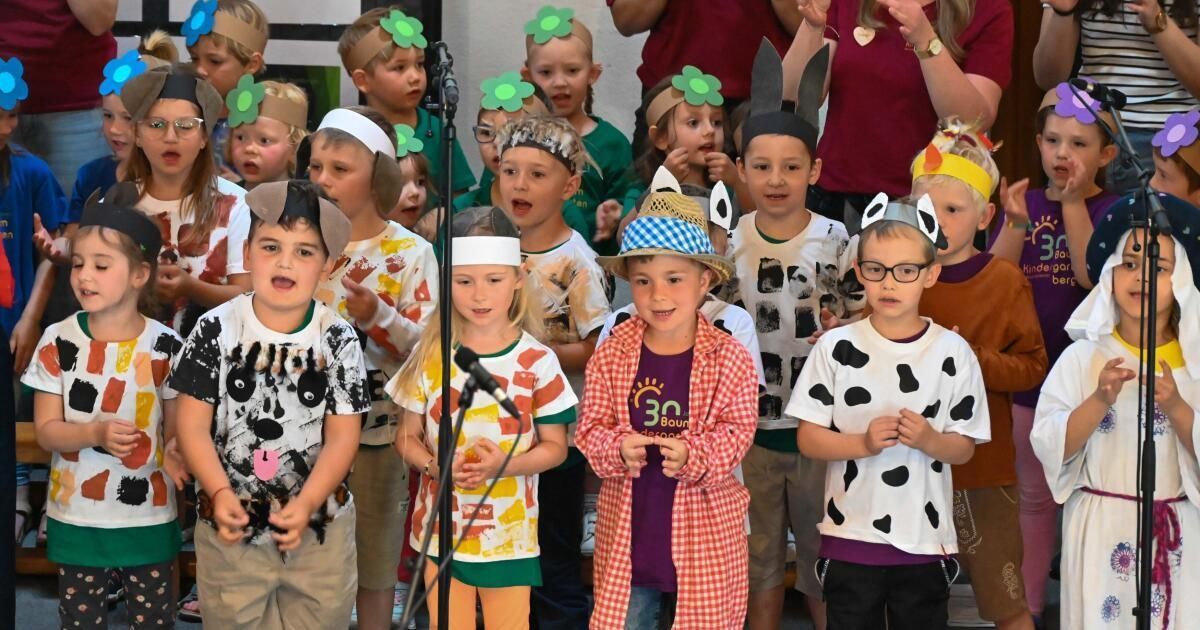 Kinder in Kostümen, darunter Tiermützen, singen vor einem Mikrofon. Eines trägt ein Kuhkostüm, ein anderes eine Fuchsmütze.