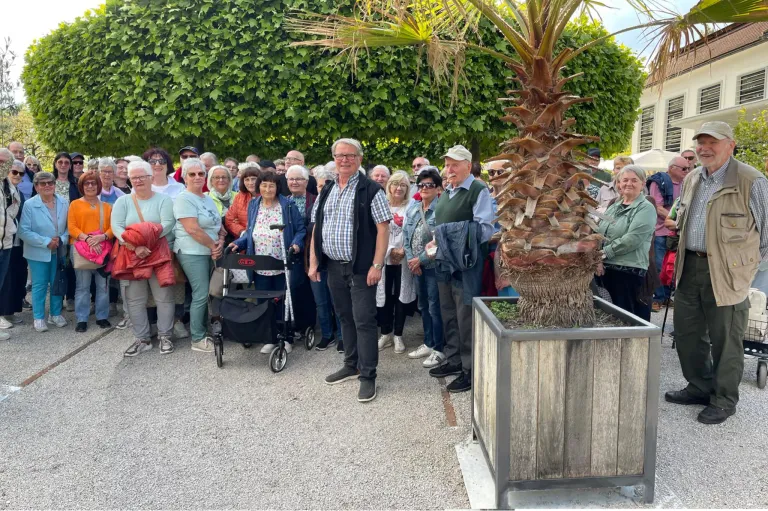 Eine Gruppe von Menschen steht draußen zusammen, wahrscheinlich bei einer Tour. Eine Person hält eine Pflanze in einem Topf.