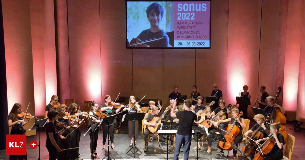 Eine Gruppe junger Musiker spielt auf der Bühne, mit einer Projektion einer Person, die Flöte spielt, im Hintergrund.