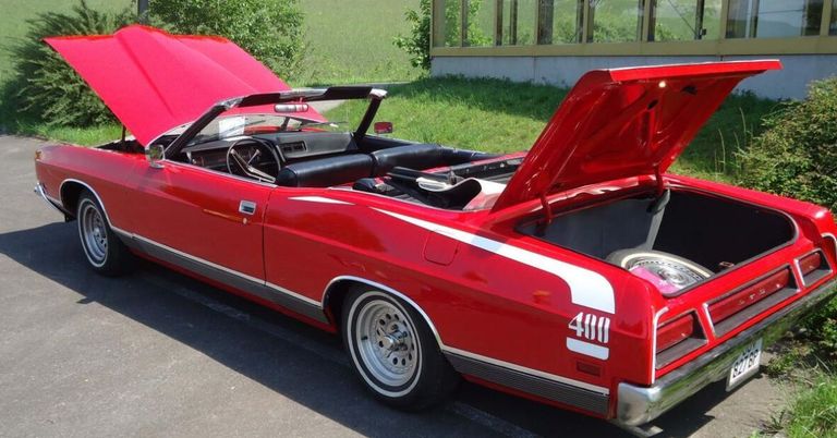 Ein roter Cabriolet mit offenem Motorhaube ist in einem grün grasbewachsenen Bereich geparkt. Es hat die Nummer 480 auf seinem Kofferraum.