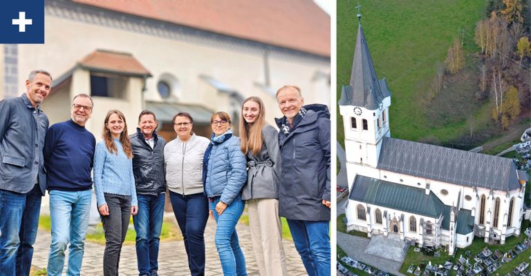 Fünf Personen lächeln und posieren für ein Foto vor einem großen Gebäude mit Rundbogenfenstern und einem Turm. Rechts ist ein Turm einer Kirche von oben zu sehen.