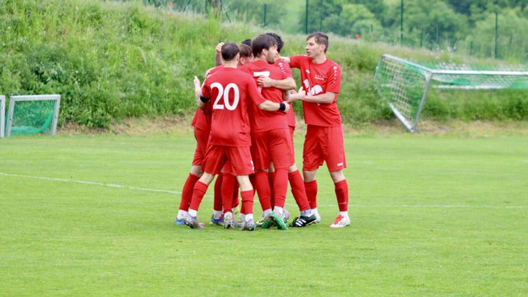 Eine Gruppe von Fußballspielern in roten Trikots feiert auf einem Feld mit einem Tor im Hintergrund.