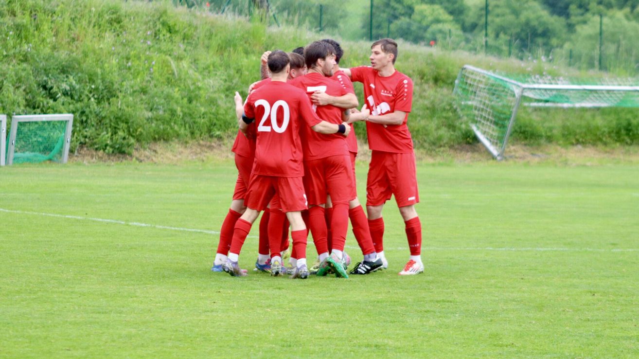 Eine Gruppe von Fußballspielern in roten Trikots feiert auf einem Feld mit einem Tor im Hintergrund.