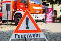Ein Warnschild mit Ausrufezeichen weist auf einen Feuerwehrwagen im Hintergrund hin und signalisiert die Anwesenheit der Feuerwehr.