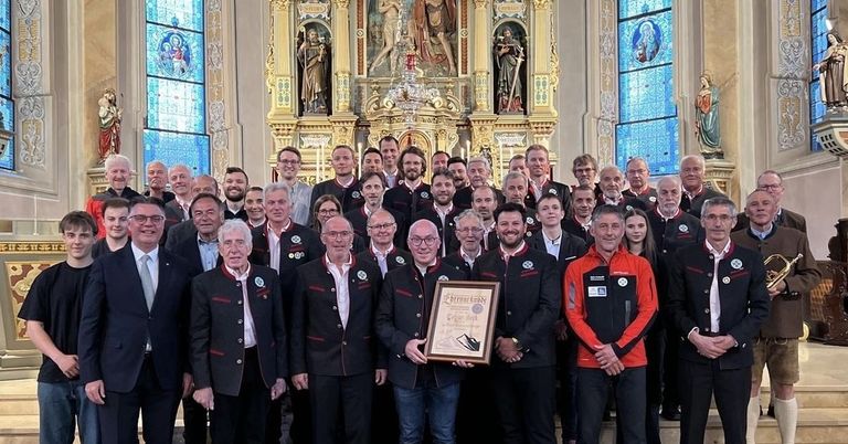 Eine Gruppe von Menschen, wahrscheinlich ein Sportteam, posiert für ein Foto in einer Kirche. Ein Mann in der Mitte hält eine Plakette.