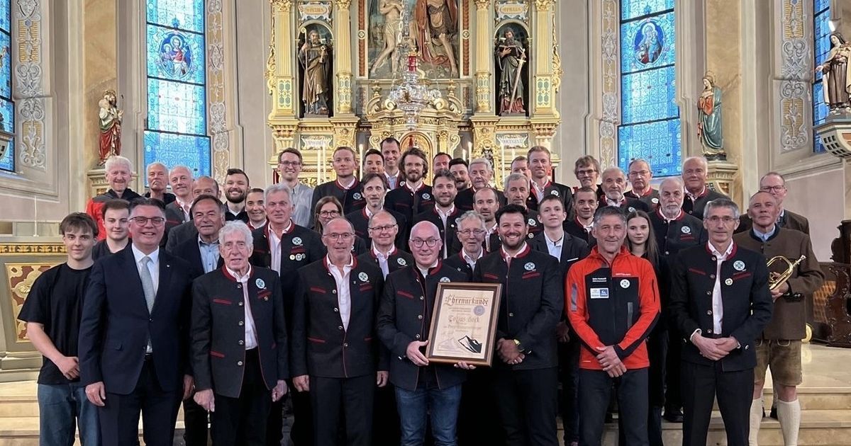 Eine Gruppe von Menschen, wahrscheinlich ein Sportteam, posiert für ein Foto in einer Kirche. Ein Mann in der Mitte hält eine Plakette.