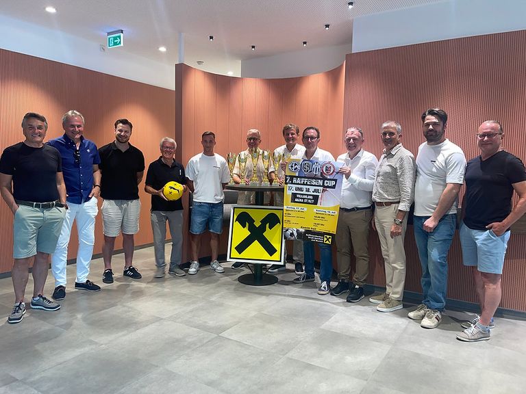 Group of men stand together holding trophies and a soccer ball. A yellow banner with black text reads 7. RAFFELSEEN CUP.