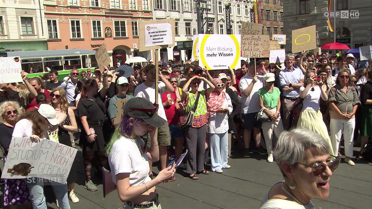 Eine Menschenmenge von Demonstranten versammelt sich im Freien und hält Schilder hoch, die für mehr Bildungsfinanzierung werben. Einige Schilder tragen die Aufschrift 'Mehr Bildung, mehr Wissen' und 'Zählen Studenten?' während andere die aktuelle Budgetzuteilung kritisieren.