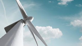 A close-up of a wind turbine's blades and tower under a blue sky with scattered clouds. The blades are white with a smooth surface, and the tower is white with a round base.