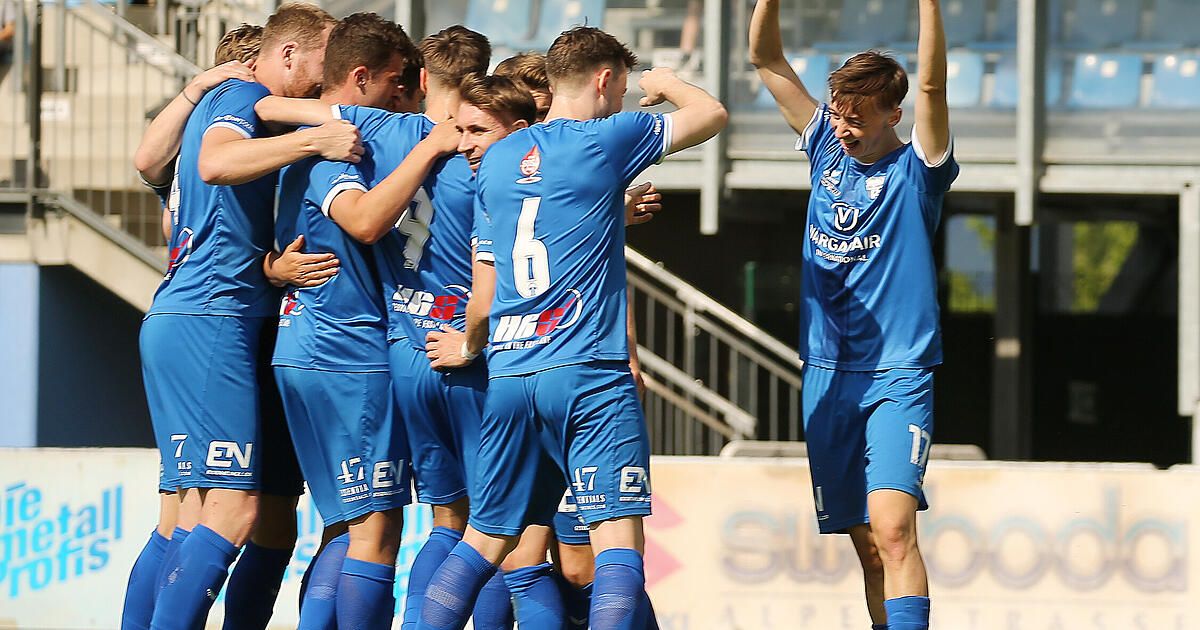 A group of young men in blue jerseys celebrate a victory on a sports field. One player, number 6, stands with his arms raised.