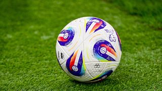 Ein Fußball mit Regenbogendesign und mehreren Aufnähern liegt auf einem grünen Rasen. Er hat eine weiße Basis mit mehrfarbigen Aufnähern.