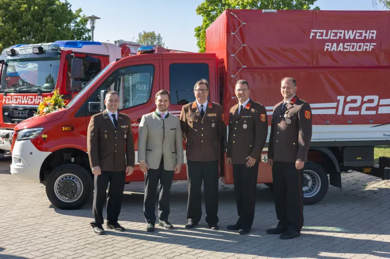 Fünf Männer in Uniformen stehen vor einem roten Feuerwehrauto. Sie scheinen für ein Foto zu posieren.