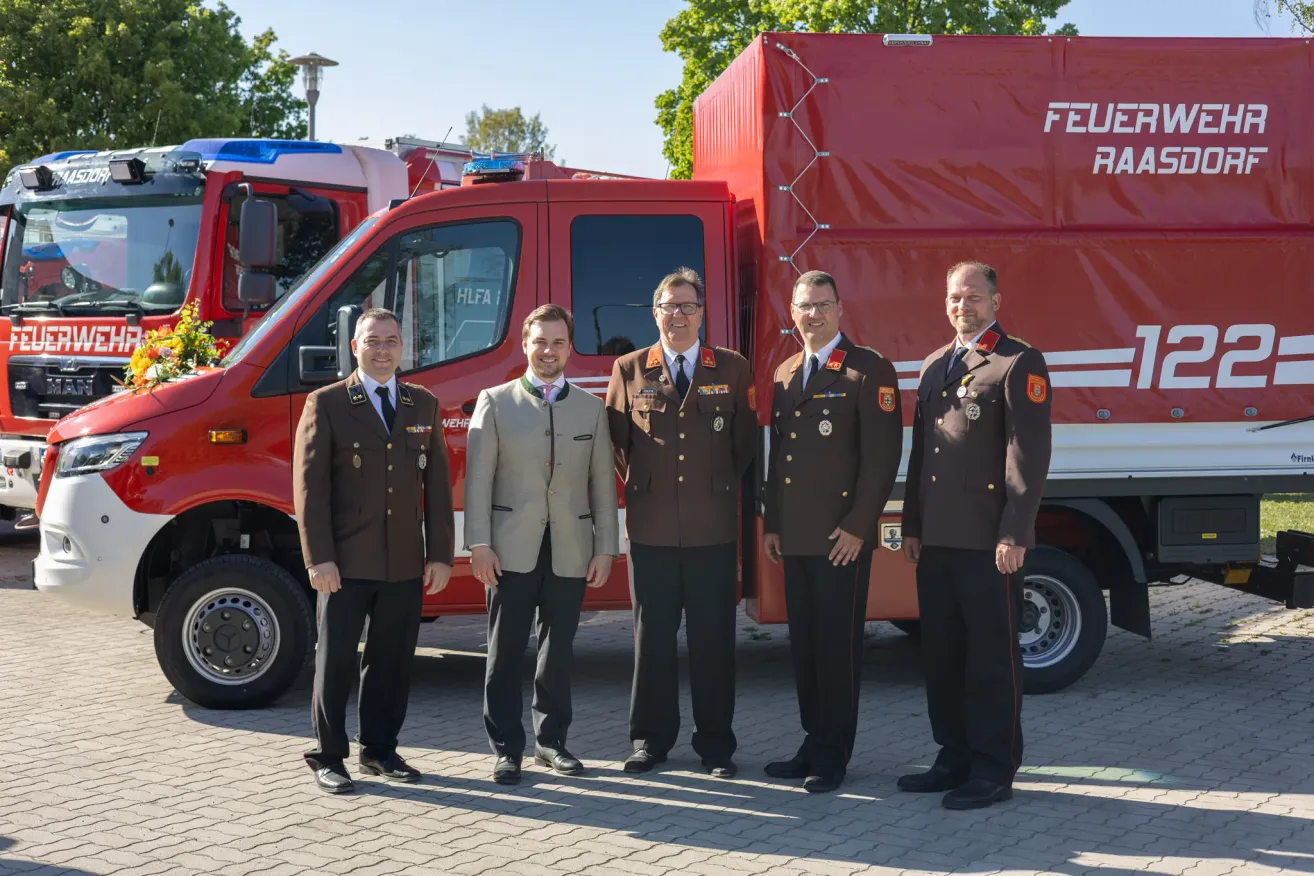 Fünf Männer in Uniformen stehen vor einem roten Feuerwehrauto. Sie scheinen für ein Foto zu posieren.