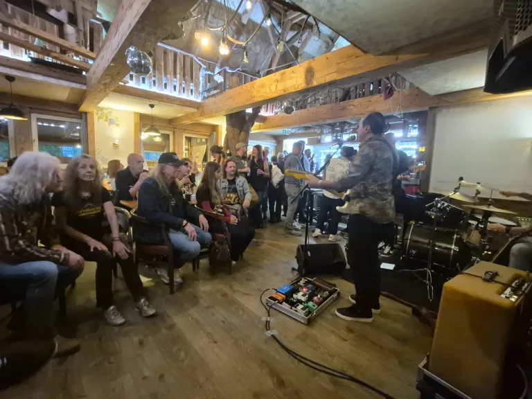 Eine Band spielt auf der Bühne in einem Restaurant. Der Musiker spielt die Gitarre, während andere Schlagzeug und andere Instrumente spielen. Die Leute sitzen in Stühlen um die Bühne herum und sehen sich die Aufführung an.