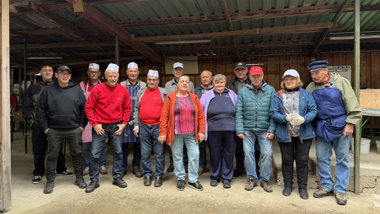 A group of people in hats and gloves pose for a photo inside a barn. They wear various colored shirts and pants.