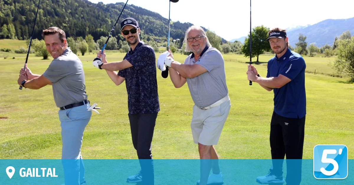 Vier Männer sind auf einem Golfplatz. Sie halten Golfschläger und posieren für ein Foto. Der Hintergrund zeigt Bäume und Berge.