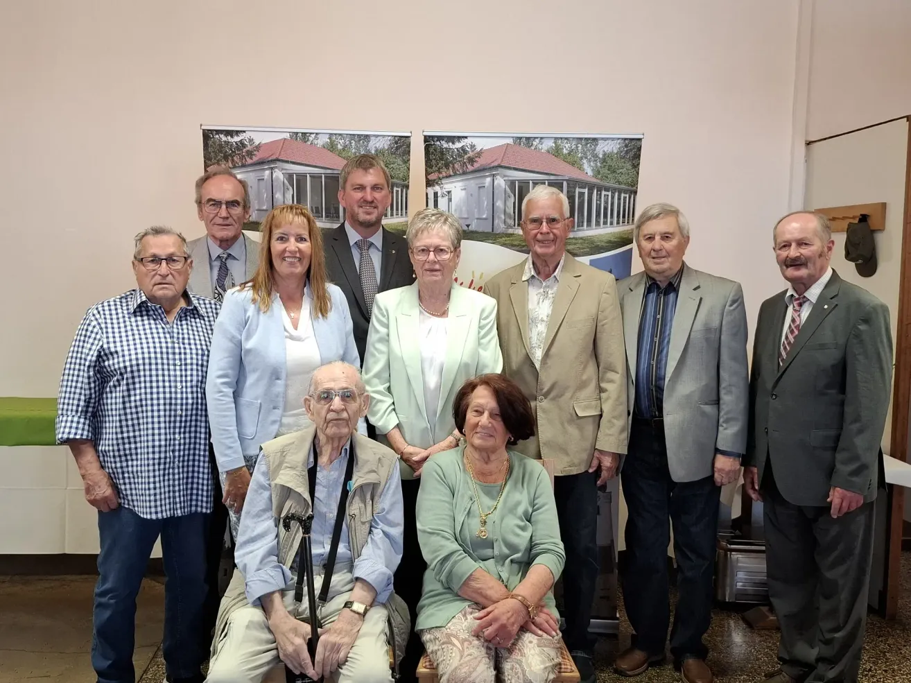 Eine Gruppe älterer Menschen steht vor einer Wand mit Hausgemälden, lächelt und posiert für ein Foto.