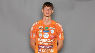 A man stands in an orange sports jersey with various sponsor logos, including Admiral, Thau Coco, and others.